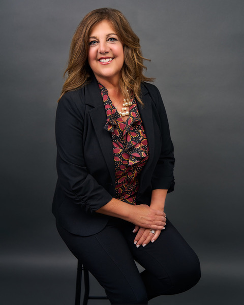 Maria Sainz seated for a studio portrait, warm neutral backdrop, calm and direct expression to camera.
